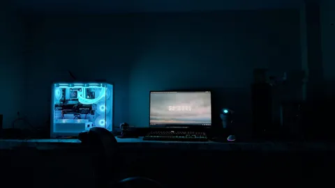 Dark gaming room with a glowing glass-sided PC case and a monitor on a long desk
