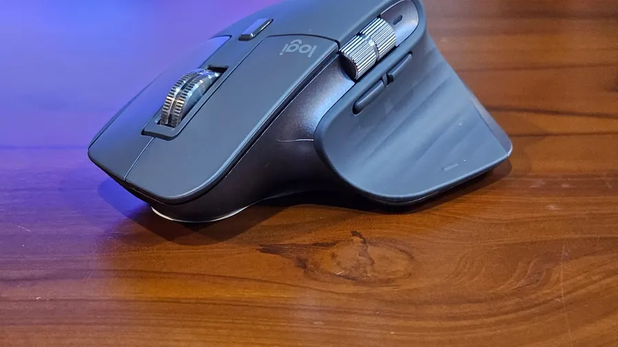Grey ergonomic mouse with thumb buttons on a wooden desk