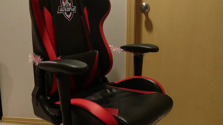 Black and red racing-style gaming chair with padded armrests in a bedroom