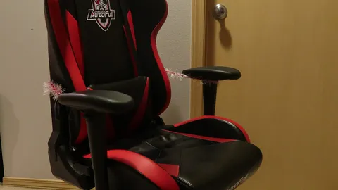 Black and red racing-style gaming chair with padded armrests in a bedroom