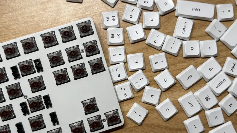 Mechanical keyboard with keycaps removed, exposing brown switches, next to scattered white keycaps