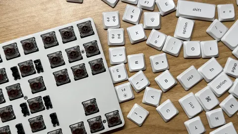 Mechanical keyboard with keycaps removed, exposing brown switches, next to scattered white keycaps