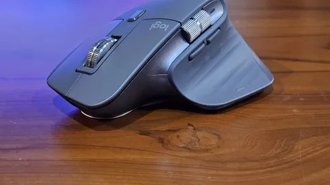 Grey wireless computer mouse resting on a wooden table under blue light