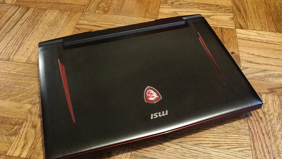 Closed black MSI gaming laptop with red accents lying on a parquet wood floor