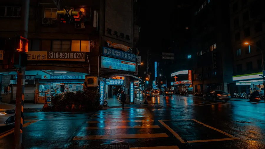 City street at night with neon shop signs reflected on wet pavement