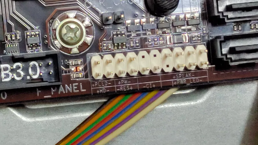 Close-up of a desktop motherboard's front panel header with a multicoloured ribbon cable attached, next to a clear CMOS jumper