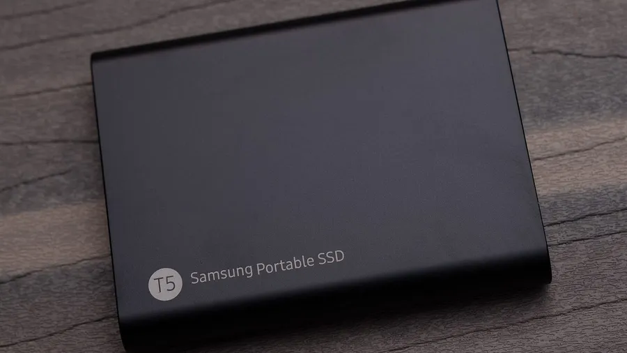 Black Samsung T5 portable SSD lying on a dark wooden surface
