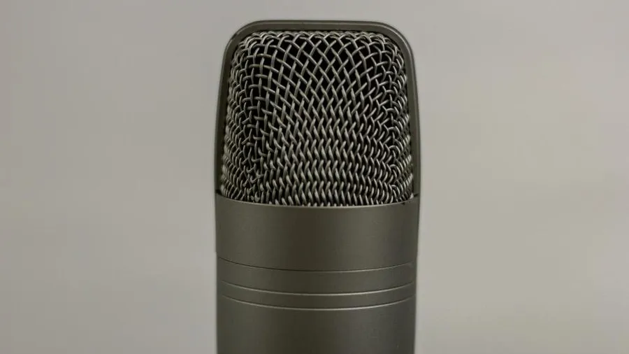 Close-up of a studio condenser microphone against a gray background